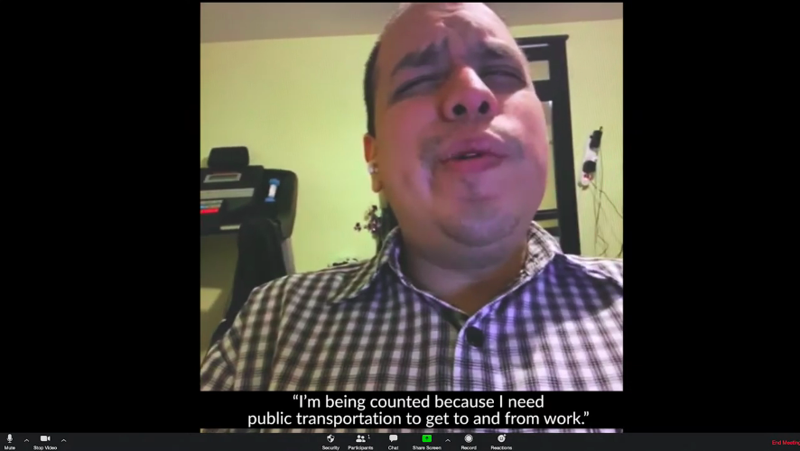 Screenshot of a video conference call of a man wearing a plaid button up shirt. The closed captioning on reads I'm being counted because I need public transportation to get to and from work.